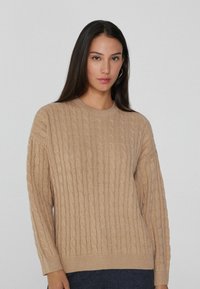 Beige gestrickter Pullover mit einem strukturierten Zopfmuster, Rundhalsausschnitt und langen Ärmeln. Das Material wirkt weich und leicht.