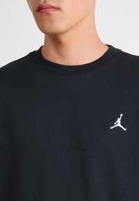 Schwarzer Baumwollpullover mit Rundhalsausschnitt und einem weißen Jumpman-Logo, das auf der linken Brustseite gestickt ist. Glatte Textur.