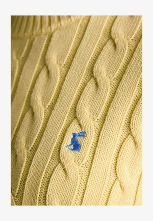 Geltonos spalvos megztinis audinys su mažu mėlynu siuvinėtu triušiuko logotipu, integruotu į mezgimo raštą.