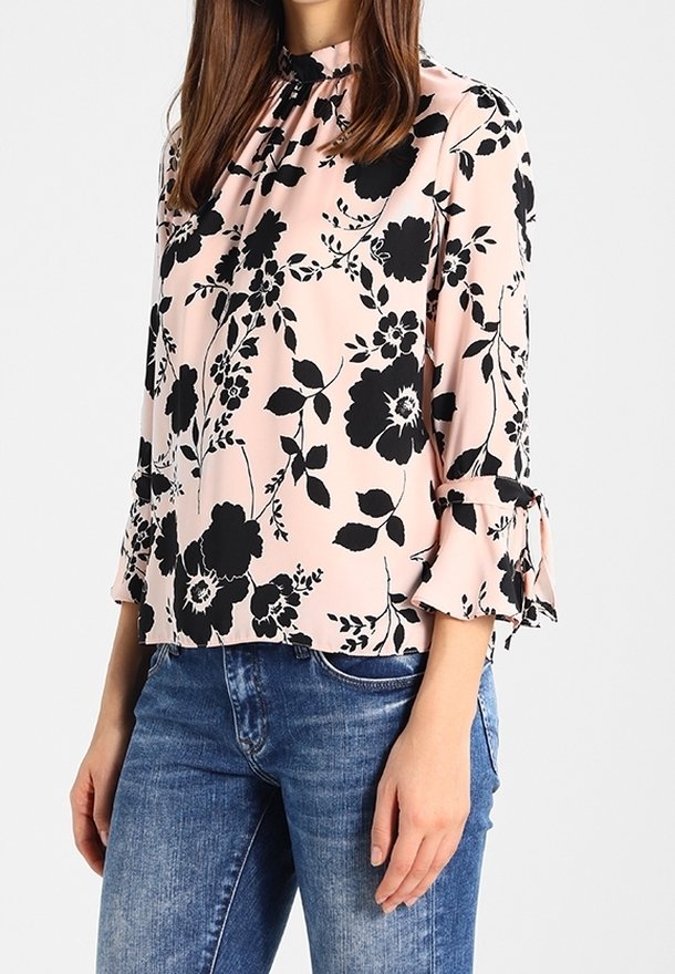 Blusa floreale in rosa chiaro con motivi neri. Presenta maniche lunghe con polsini arricciati e scollatura arricciata. Abbinarla a jeans blu.