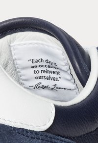 Intérieur de basket avec une étiquette en tissu blanc portant la citation : "Chaque jour est une occasion de se réinventer." - Ralph Lauren.