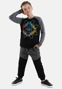 Svart och grå långärmad tröja med en grafik av en videospelkontroll; matchad med grå och svarta mjukisbyxor; svarta sneakers.