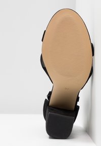 Chaussure à talon haut noire avec une tige en tissu texturé, montrant une semelle beige lisse. Caractérisée par un talon carré et une taille indiquée 37.