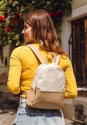 Small cream and tan backpack with a smooth texture, rounded top, gold zipper, and subtle dot pattern. Adjustable straps and top handle.
