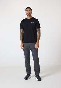 Schwarzes Baumwoll-T-Shirt mit kleinem "Classic Life"-Text auf der Brust, kombiniert mit grauen Cargo-Hosen und schwarzen Sport-Sneakern.