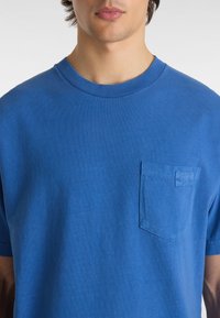 Camiseta de algodón azul de manga corta con cuello redondo y un bolsillo en el pecho izquierdo. Textura suave y corte clásico.
