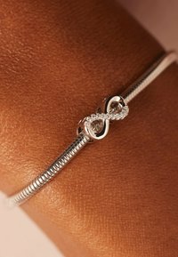 Silver bracelet with a flexible snake chain, featuring an infinity symbol clasp embedded with small clear gemstones.