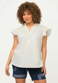 Blouse blanche avec des manches volantes, design col, et fente à l'avant. Associée à un short bleu marine avec un motif et une garniture décorative.