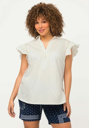 Hvid bluse med flæsekirtler, krave-design og frontslids. Parret med navy shorts med mønster og dekorativ kant.