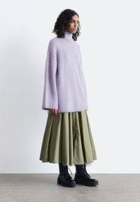 Lavender oversized sweater in soft, fluffy material with a high neck, paired with a green pleated skirt and black lace-up boots.