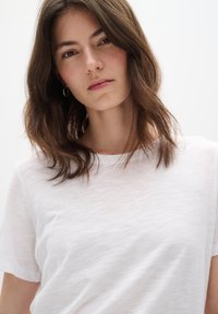 Tricou alb cu mânecă scurtă, confecționat dintr-un material moale, ușor texturat. Decolteul este de tip crew și tăietura este lejeră.