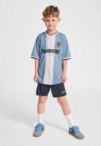 Ljusblå sporttröja med vit rand, "hummel"-logotyp, svarta detaljer; matchas med marinblå shorts och blå sneakers, vita strumpor.