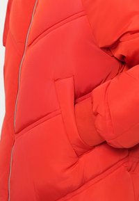 Piros puff jacket steppelt dizájnnal, cipzáras elülső rész és oldalsó zsebek. Jellemzője a bordázott csuklórész és a sima textúra.