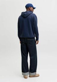 Navy hoodie with a drawstring hood, paired with dark denim pants featuring rolled cuffs. Light brown boots complete the outfit.