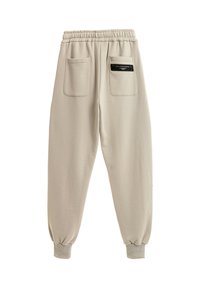 Pantalones de chándal beige con cinturilla elástica, dos bolsillos traseros y puños acanalados en los tobillos. Tejido suave con una textura lisa.