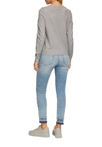 Grijze lange mouw top met een ronde hals, gecombineerd met lichtblauwe skinny jeans met een rafelige zoom, en lichtgrijze sneakers.