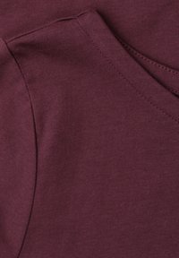 Gros plan d’un tissu bordeaux avec des coutures visibles et un détail de couture pliée.