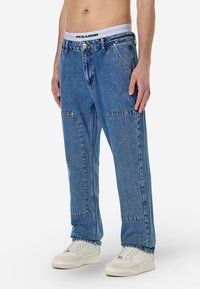 Vaaleansiniset rentomalliset farkut, joissa on suuret etutaskut ja hillityt ompeludetaljit. Yhdistetty valkoisiin tennareihin.