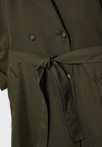 Trench-coat vert foncé avec boutons croisés et ceinture en tissu nouée à la taille, avec poches latérales.