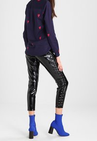 Schwarze glänzende Leggings mit Schnürdetails, kombiniert mit einem marineblauen Shirt mit roten Herzmustern und blauen Ankle-Boots mit Blockabsätzen.