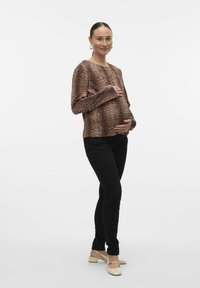 Majica dugih rukava s leopard uzorkom, mekani materijal, uparen s crnim uskim hlačama i svijetlim balerinkama. Model drži rastući trbuh.