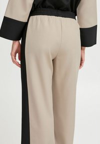 Pantalons taille haute en mélange de tissu beige et noir. Dotés d'une taille élastique froncée et de panneaux latéraux contrastants. Texture lisse.