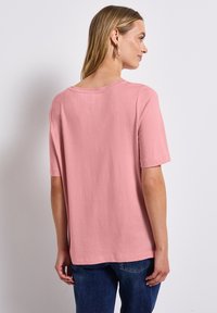 Svetle růžové tričko s krátkým rukávem vyrobené z měkké bavlny, s kulatým výstřihem a volným střihem, s viditelnými švy podél lemu.