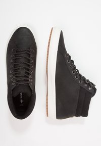 Svarta högskodda sneakers med en texturerad läderutsida, gummisula, vit mellansula och svarta snörningsdetaljer. Har vadderad krage.