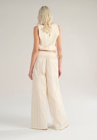 Top beige senza maniche a righe verticali, abbinato a pantaloni a gamba larga di colore chiaro, con una vestibilità comoda e vita elasticizzata.