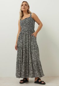 Maxiklänning med smockad byst, svart och vit zebra-mönster, breda axelremmar, volangkjol och sidofickor. Accessoriseras med svarta sandaler.