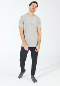 Grå kortærmet t-shirt med et tekstureret mønster, kombineret med sorte tætsiddende bukser og grå athletic sko, sat mod en lys baggrund.