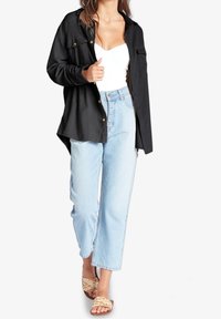 Camicia nera con bottoni e texture a coste, jeans dritti azzurri chiari e sandali intrecciati con una palette di colori naturali.