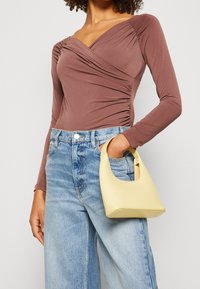 Langärmliger bordeauxfarbener Bodysuit mit gerafftem Seitendetail, kombiniert mit hochtaillierten hellblauen Jeans und einer gelben Handtasche mit gebogenem Griff.