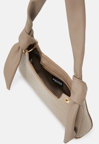 Beige käsilaukku, jossa on teksturoitu krokotiilikuosi, pehmeä materiaali ja solmittu kangaskahva. Kultaiset metalliosat näkyvissä aukossa.