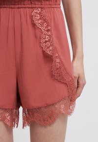 Shorts de couleur framboise avec une taille élastique, présentant un elegant bord en dentelle sur les côtés et l'ourlet. Tissu doux avec une texture lisse.