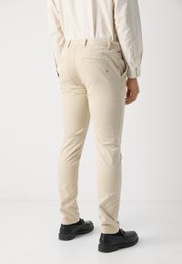 Chinos en coton beige avec une coupe slim, dotés de poches arrière, de détails de couture subtils et de chaussures noires. Texture lisse et design ajusté.