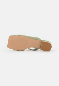 Sandalo verde con tacco e apertura sul retro, caratterizzato da un materiale superiore liscio, una suola in gomma testurizzata e un fondo beige solido.