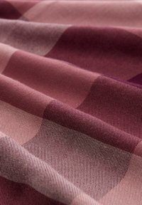 Textiel met een golfpatroon in tinten mauve en bordeaux, met een gestructureerde oppervlakte en zichtbare geweven details, waardoor diepte en dimensie ontstaat.