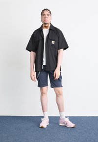 Svart kortermet skjorte med lomme, hvit t-skjorte med rund hals, marineblå cargo-shorts og rosa joggesko med hvite sokker.