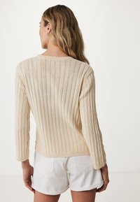 Ljust beige ribbat tröja med långa ärmar och rund halsringning, kombinerad med vita shorts. Har en mjuk textur och en åtsittande design.