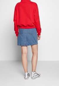 Rode sweatshirt met een hoge hals, blauwe denim mini-rok en witte hoge sneakers met zwarte tekst en grafische accenten.