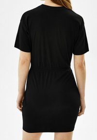 Musta lyhythihainen mekko, jossa on joustava vyötärö, yksinkertainen muotoilu ja sileä pinta. Takana on pyöreä pääntie ja tiukka siluetti.