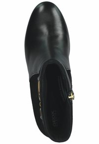 Stivale alla caviglia in pelle nera con finitura liscia, punta tonda e hardware decorativo in oro sul lato. L'interno presenta un'etichetta "PASSIONATE COMFORT".