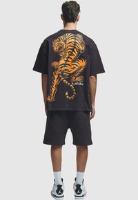 Camiseta negra de gran tamaño con un gráfico de tigre naranja en la parte posterior. Combinada con pantalones cortos a juego y zapatillas en blanco y negro. Textura de algodón suave.