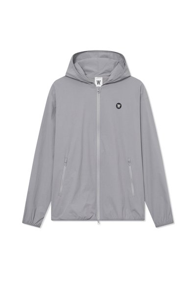 Veste grise clair avec capuche, fermeture éclair à l'avant, deux poches latérales et un petit logo noir sur la poitrine. Fabriquée en tissu léger et lisse.