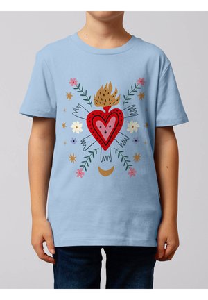 Kind trägt hellblaues T-Shirt mit rotem flammendem Herz, umgeben von weißen Händen, Blumen, Sternen, grünen Zweigen und einem goldenen Halbmond.