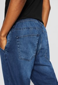 Pantalones de mezclilla en azul oscuro con una cintura elástica, bolsillos traseros visibles y una textura suave. Corte recto con detalles de costura.