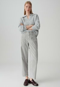 Maglione oversized grigio chiaro con scollo a V e colletto, abbinato a pantaloni larghi grigi con tasche applicate e una texture morbida.
