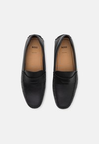 Mocassins en cuir noir avec une texture lisse, bout arrondi, couture décorative et logo de la marque à l'intérieur. Fabriqués en Europe.