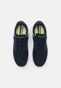 Laivastonsiniset verkkokengät valkoisella pohjalla, joissa on teksturoitu pinta, nauhakiinnitys ja huomaamattomat punaiset ja valkoiset yksityiskohdat kielen alueella.